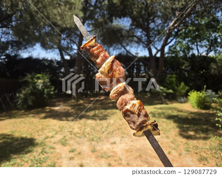 Outdoor summer barbecue featuring grilled meat skewer in sunny backyard setting. Horizontal banner. Copy space Outdoor summer barbecue featuring grilled meat skewer in sunny backyard setting. Horizontal banner. Copy space 129087729