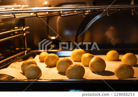 Golden sweet cookies baking in a hot oven, rising and spreading on a baking tray. Golden sweet cookies baking in a hot oven, rising and spreading on a baking tray. 129088253
