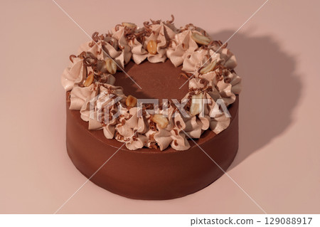 Round bento cake with chocolate frosting and decorative whipped cream topping, featuring nuts and chocolate shavings, beautifully presented on a soft pink background, ideal for celebrations and 129088917