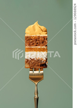 Colorful bento carrot cake slice with orange and mango filling, held by a golden fork, showcasing layers of sponge, cream, and frosting against a soft green background Colorful bento carrot cake slice with orange and mango filling, held by a golden fork, showcasing layers of sponge, cream, and frosting against a soft green background 129088924