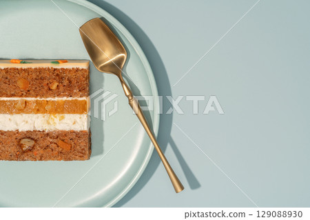 Bento carrot cake slice with orange and mango filling, displayed on a pastel plate with a golden serving spoon, showcasing layers of cake and cream, emphasizing the delightful cross-section 129088930
