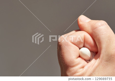 close up of caucasian adult hand holding a white pill against a neutral 129089735