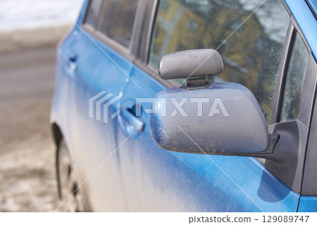 close up of dirty blue car with snowy ground and blurred background 129089747