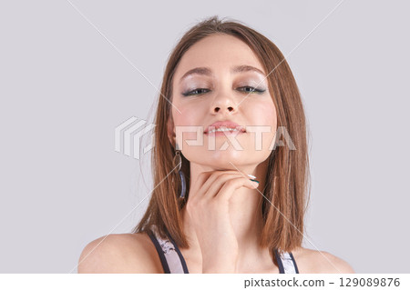 Confident young caucasian female posing with hand on chin against neutral 129089876