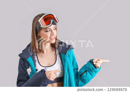 Young caucasian female in ski gear pointing with fingers in stylish winter Young caucasian female in ski gear pointing with fingers in stylish winter 129089878