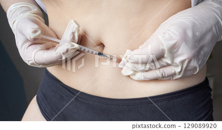 Hispanic female administering insulin injection in abdomen with gloves 129089920