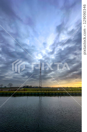 A stunning dramatic sky reflects beautifully over calm water, featuring a communication tower A stunning dramatic sky reflects beautifully over calm water, featuring a communication tower 129090346