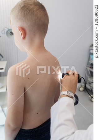 A pediatric dermatologist examining a young boys skin with a dermatoscope in a medical clinic. Skin check up for moles and birthmarks. 129090622
