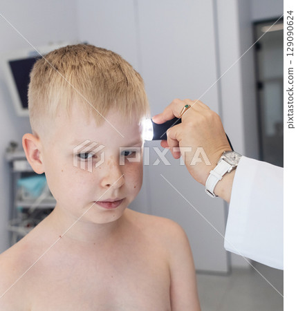 A pediatric dermatologist examining a young boys skin with a dermatoscope in a medical clinic. Skin check up for moles and birthmarks. 129090624