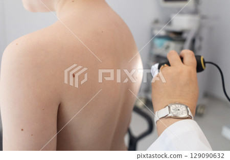 A pediatric dermatologist examining a young boys skin with a dermatoscope in a medical clinic. Skin check up for moles and birthmarks. 129090632