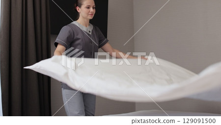 Chambermaid makes bed in hotel bedroom. Cleaning service in hotel rooms, hotel business. 129091500