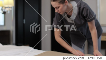 Woman housekeeper preparing bed clothes in the hotel room. Cleaning service in hotel rooms, hotel business. 129091503