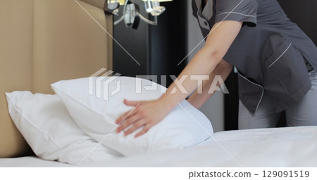 Woman housekeeper in uniform making bed for guest while cleaning hotel room. Housekeeping service in hotel room. Woman housekeeper in uniform making bed for guest while cleaning hotel room. Housekeeping service in hotel room. 129091519
