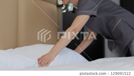 Housekeeper woman making bed and fluffing pillow in bedroom. Housekeeping service in hotel room. Housekeeper woman making bed and fluffing pillow in bedroom. Housekeeping service in hotel room. 129091522