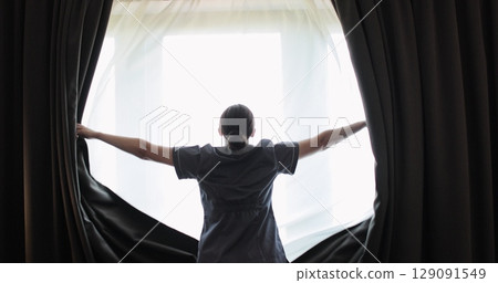 Woman housekeeper opening black curtains in hotel room. Cleaning service in hotel rooms, hotel business. 129091549