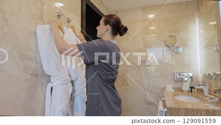 Woman hotel maid changing fresh bathrobes in room. Cleaning service in hotel rooms, hotel business. Woman hotel maid changing fresh bathrobes in room. Cleaning service in hotel rooms, hotel business. 129091559