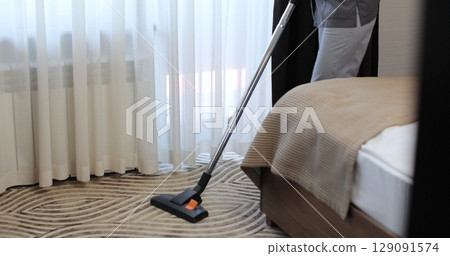 Close up woman vacuums a carpet in a hotel room. The concept of service and cleaning in the hotel room. Hotel service. Close up woman vacuums a carpet in a hotel room. The concept of service and cleaning in the hotel room. Hotel service. 129091574