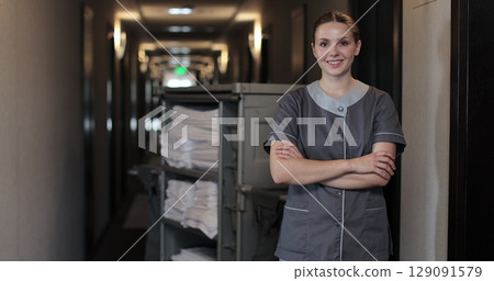 Portrait of young maid with trolley in hotel hallway, cleaning service, staff. Daily cleaning. Cleaning service in hotel rooms, hotel business. Portrait of young maid with trolley in hotel hallway, cleaning service, staff. Daily cleaning. Cleaning service in hotel rooms, hotel business. 129091579