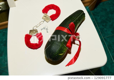 A Quirky Zucchini Styled with Handcuffs and a Colorful Ribbon on a Bathroom Floor A Quirky Zucchini Styled with Handcuffs and a Colorful Ribbon on a Bathroom Floor 129091777