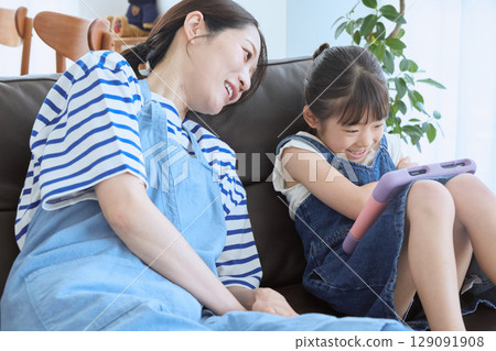 A happy moment between mother and daughter laughing on the sofa 129091908