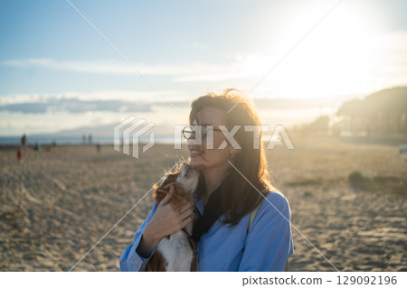 A young woman hugs her Cavalier King Charles Spaniel on the beach at sunset. Warm light, waves, and smiles capture a peaceful, joyful moment of connection and relaxation. A young woman hugs her Cavalier King Charles Spaniel on the beach at sunset. Warm light, waves, and smiles capture a peaceful, joyful moment of connection and relaxation. 129092196