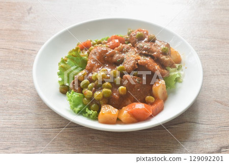 braised pork steak in gravy sauce stew with vegetable topping fresh lettuce on plate 129092201