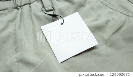 Blank white clothes tag label on gray fabric texture background 129092675