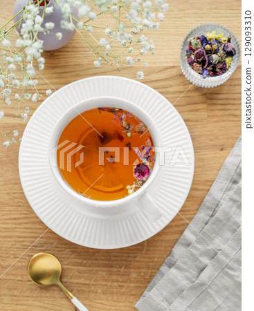 A cup of herbal tea with lemon and bouquet of flowers on a wooden table with napkin. A cup of herbal tea with lemon and bouquet of flowers on a wooden table with napkin. 129093310