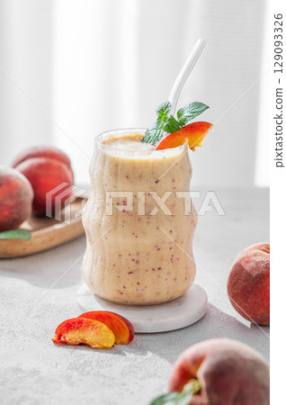 Smoothie with peach and banana in a glass on a light background near window with tropical fruits Smoothie with peach and banana in a glass on a light background near window with tropical fruits 129093326