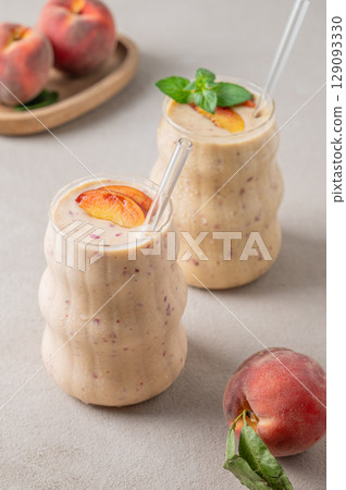 Two glasses of smoothie with peach and banana on a light background with tropical fruits. 129093330