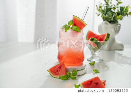 Watermelon mojito cocktail with ice and mint in a glass on a white table near window with slices Watermelon mojito cocktail with ice and mint in a glass on a white table near window with slices 129093333