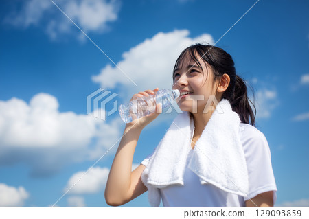 A woman hydrating under the blue sky | A moment of summer refreshment and healthy beauty A woman hydrating under the blue sky | A moment of summer refreshment and healthy beauty 129093859