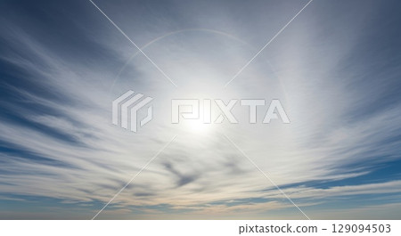 Dramatic circular cloud formation creating natural vortex pattern in blue sky with wispy white cirrus clouds swirling around bright central opening 129094503