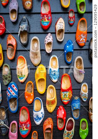 Old wooden Dutch shoes - klomps. A lot of colorful old clomps against the background of a wooden wall. Popular souvenirs. Traditions of Holland. Background 129095429