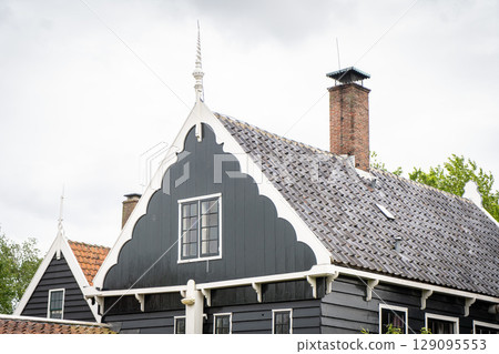 Dutch typical landscape. Traditional old dutch windmill with old houses against blue cloudy sky in the Zaanse Schans village, Netherlands. Famous tourism place. Sheep grazing on green grass. 129095553