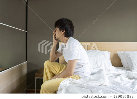 Adult Asian man sitting and feeling depressed on bed. Depression and loneliness concept. Adult Asian man sitting and feeling depressed on bed. Depression and loneliness concept. 129095882