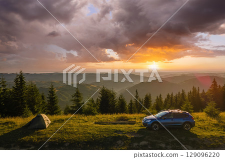 Camping tents and SUV car at mountain campsite on bright sunny evening. Active tourism and offroad concept Camping tents and SUV car at mountain campsite on bright sunny evening. Active tourism and offroad concept 129096220