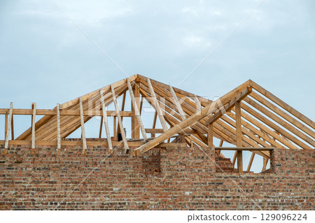 Building site with unfinished brick house with wooden roofing frame for future roof under construction. 129096224