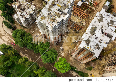 Aerial view of tower lifting crane and concrete frame of tall apartment residential buildings under construction in a city. Urban development and real estate growth concept. Aerial view of tower lifting crane and concrete frame of tall apartment residential buildings under construction in a city. Urban development and real estate growth concept. 129096347