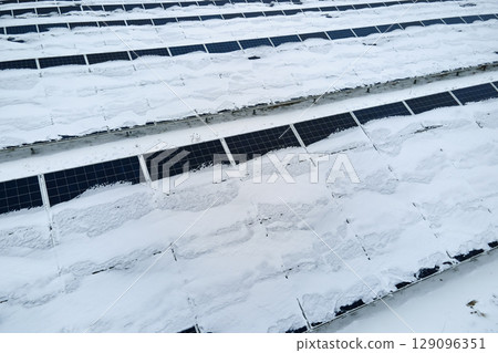 Aerial view of sustainable electrical power plant with solar photovoltaic panels covered with snow in winter for producing clean energy. Concept of low effectivity of renewable electricity in north Aerial view of sustainable electrical power plant with solar photovoltaic panels covered with snow in winter for producing clean energy. Concept of low effectivity of renewable electricity in north 129096351