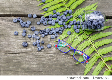 Eco friendly, food, summer composition with organic, wild blueberries and kid eyeglasses on a wooden table with fern leaf. Natural blueberries are a source of vitamins and nutrient for good vision 129097979