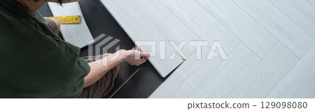 A man lays a quartz laminate on the floor. Renovation, Installation of French herringbone, banner 129098080