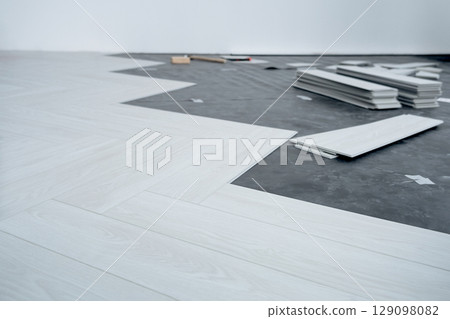 A man lays a quartz laminate on the floor. Renovation, Installation of French herringbone A man lays a quartz laminate on the floor. Renovation, Installation of French herringbone 129098082