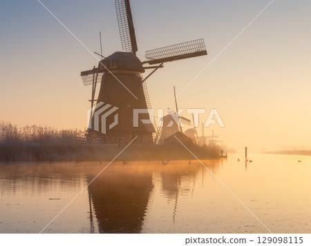 Windmills in the Netherlands during sunrise. Foggy morning and sunshine. Dutch canals. 129098115