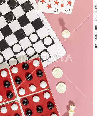 Board games. Various board games with chess pieces, checkers and playing cards on a pink background. Vacation at home with family. Free time with table game. Flat lay 129098450