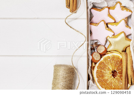 Hande made present with home made cookies, dry fruits, nuts and cinnamon stiks on a white wooden background with copy space. Winter holiday pastries. Christmas cookies. Hand made gifts. Flat lay 129098458