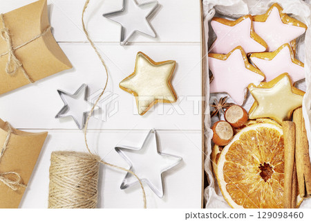 Hande made presents with home made cookies, dry fruits, nuts and cinnamon stiks on a white wooden background. Winter holiday pastries. Christmas cookies. Hand made gifts. Flat lay 129098460