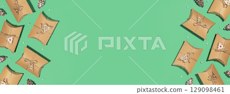 Christmas eco friendly banner. Craft gift boxes with decoration on a green background with empty place for text. Christmas, winter holiday, new year concept. Flat lay, copy space, banner size Christmas eco friendly banner. Craft gift boxes with decoration on a green background with empty place for text. Christmas, winter holiday, new year concept. Flat lay, copy space, banner size 129098461