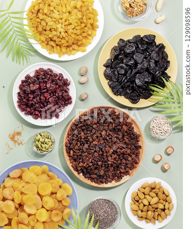 Dry fruits, nuts and seeds assortment on a blue background with palm leaves. Healthy snack - mix of organic nuts and dry fruits. Vegan and vegetarian products. Flat lay 129098596