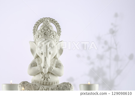 Sculpture of Lord Ganesha with candles on a gradient light background with shadows and copy space. Holiday of Ganesh Chaturthi. Ganesh festival. Hindu religion holidays. Front view Sculpture of Lord Ganesha with candles on a gradient light background with shadows and copy space. Holiday of Ganesh Chaturthi. Ganesh festival. Hindu religion holidays. Front view 129098610